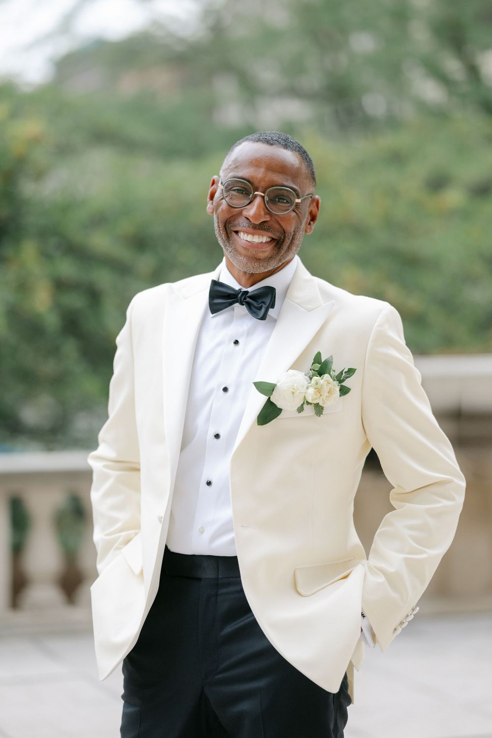 A groom in a cream tuxedo jacket and black bow tie smiles warmly during an outdoor wedding. - The Art Institute of Chicago Wedding
