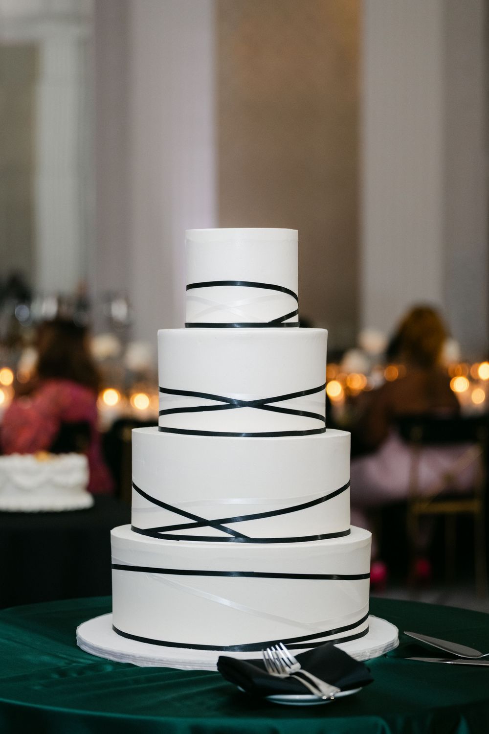 Modern white wedding cake with elegant black ribbon design on a green tablecloth at a reception venue. - Midland Hotel Chicago Wedding