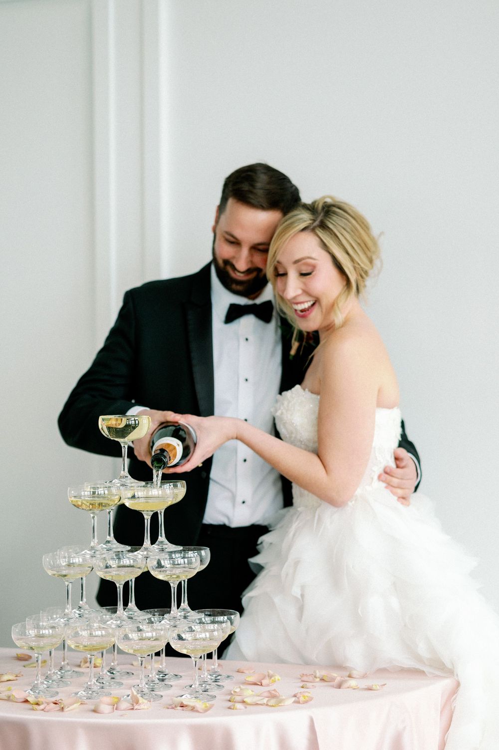 A couple pours champagne into a tower of elegant crystal glasses during their wedding celebration.