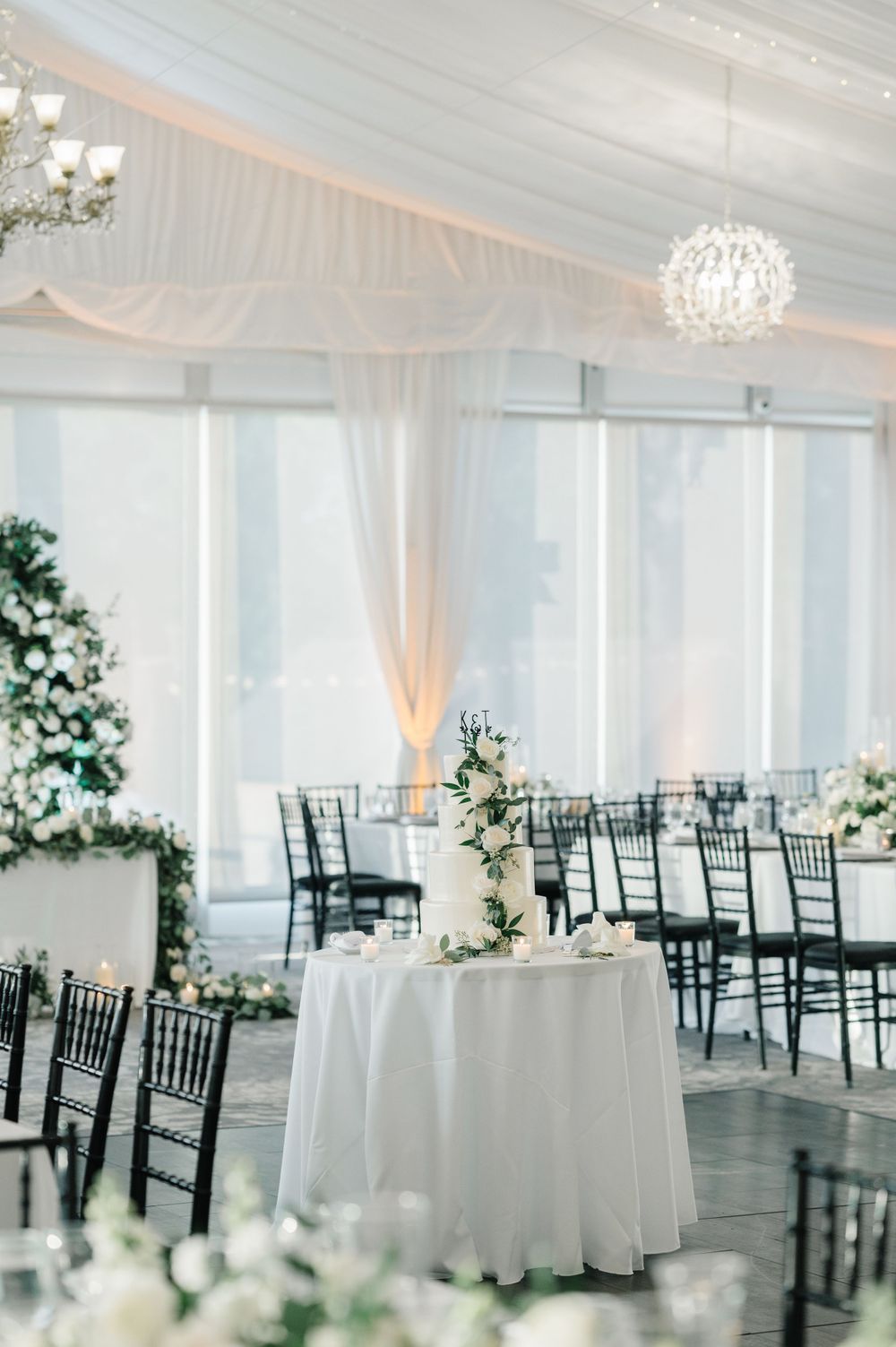 Elegant white wedding reception venue with crystal chandelier, black chiavari chairs and floral centerpieces. - Monte Bello Estate Wedding