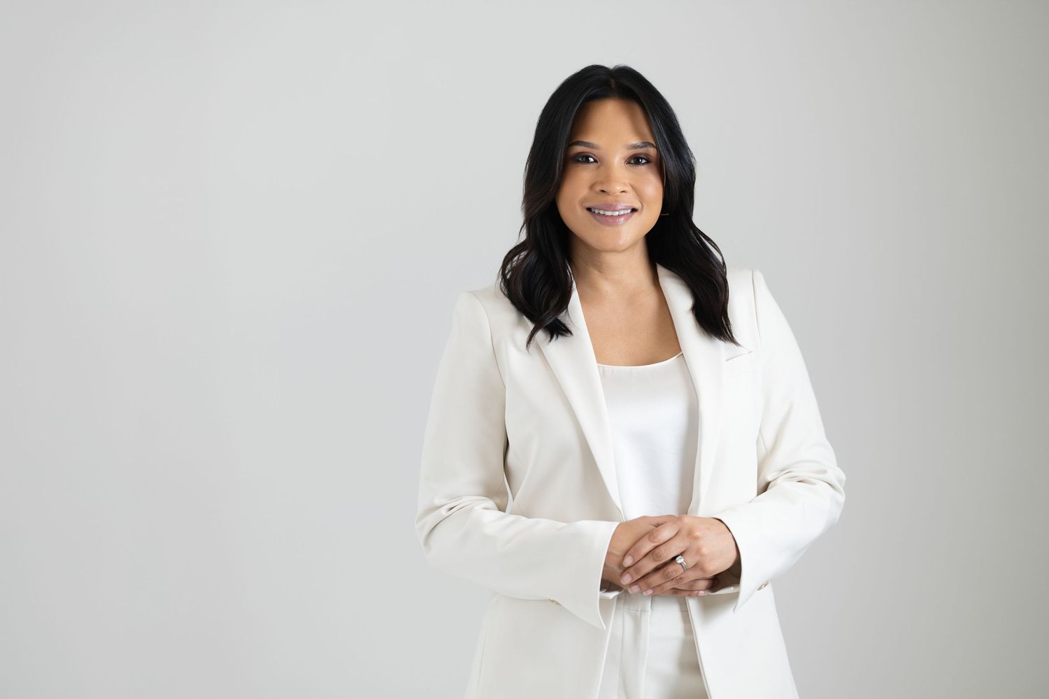 Professional wearing a crisp white blazer and top stands confidently against a light gray background.