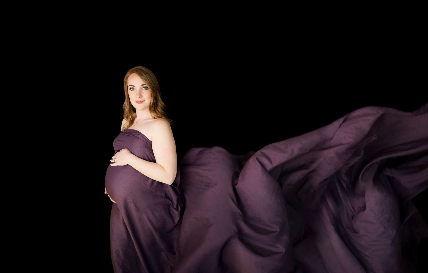 Artistic portrait with flowing purple fabric against dark background.