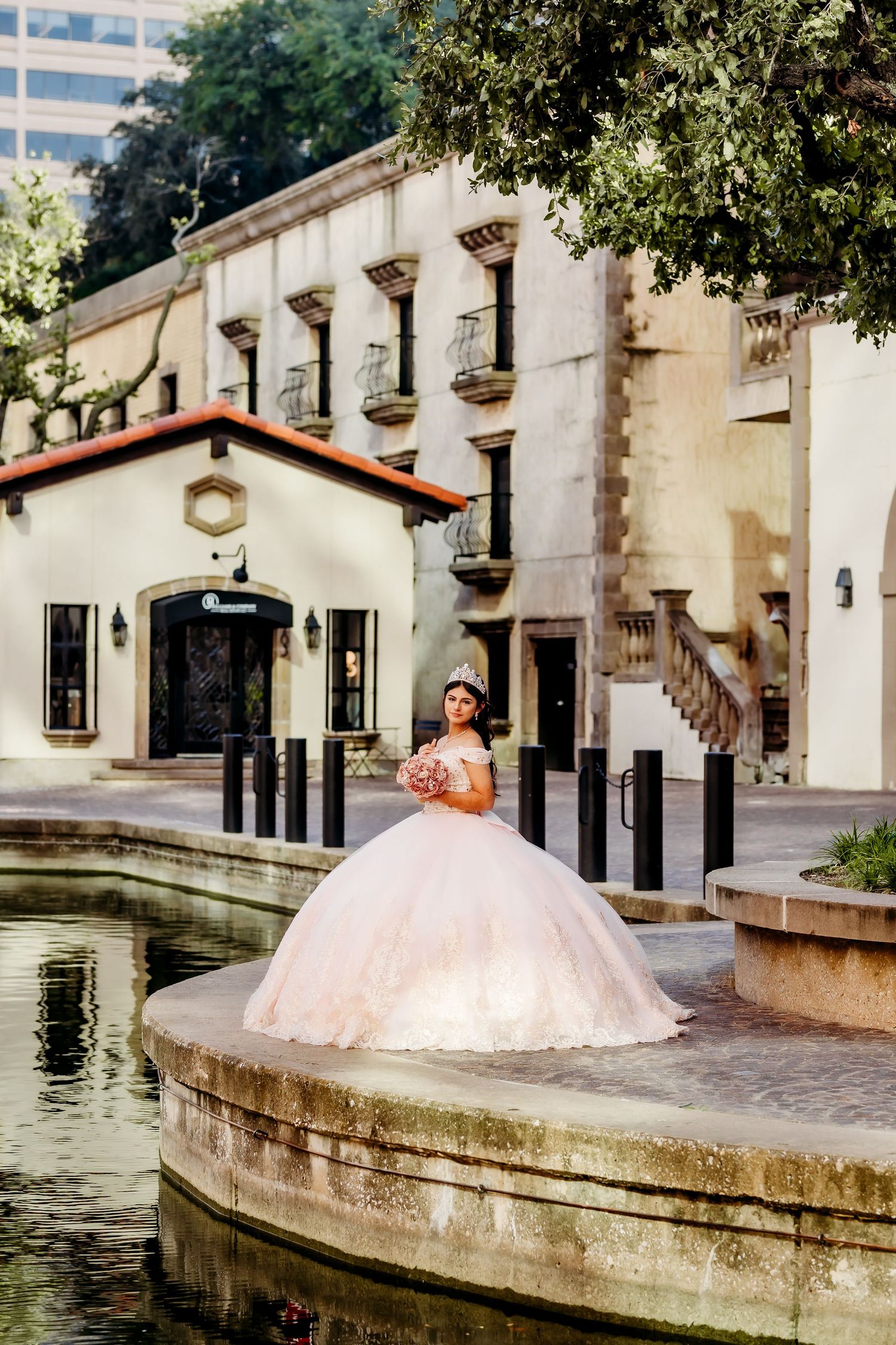 Pink ballgown photoshoot at a historic building with water fountain and stone architecture.