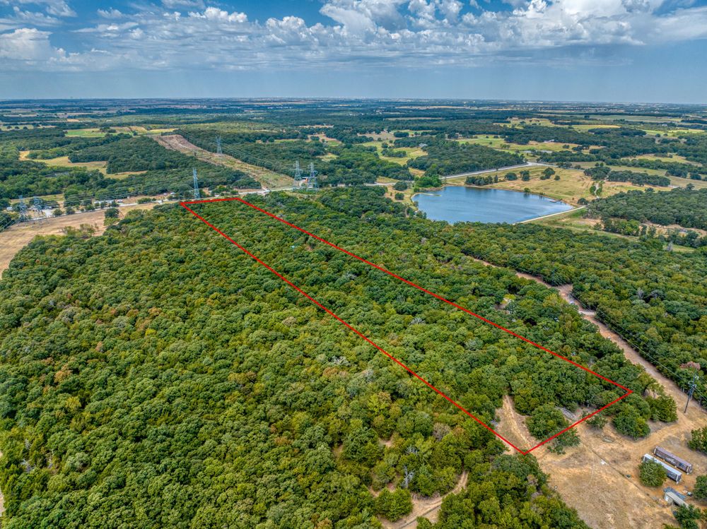 Aerial view of dense forest surrounding a lake with winding roads through countryside.