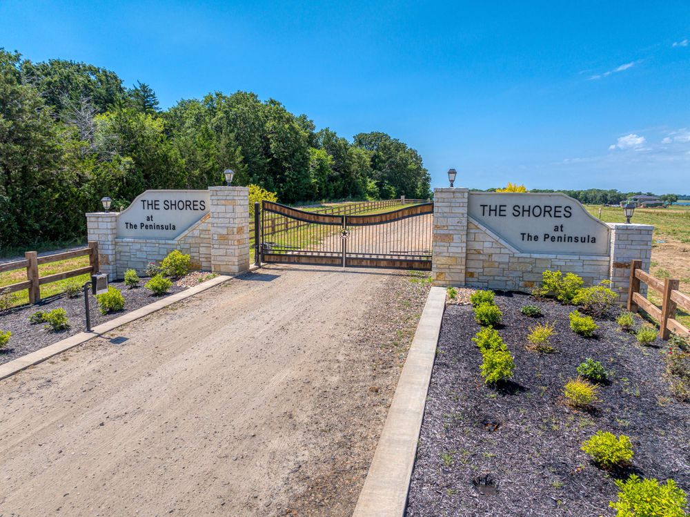 Gated entrance to The Shores development with landscaped stone signage and dirt road.
