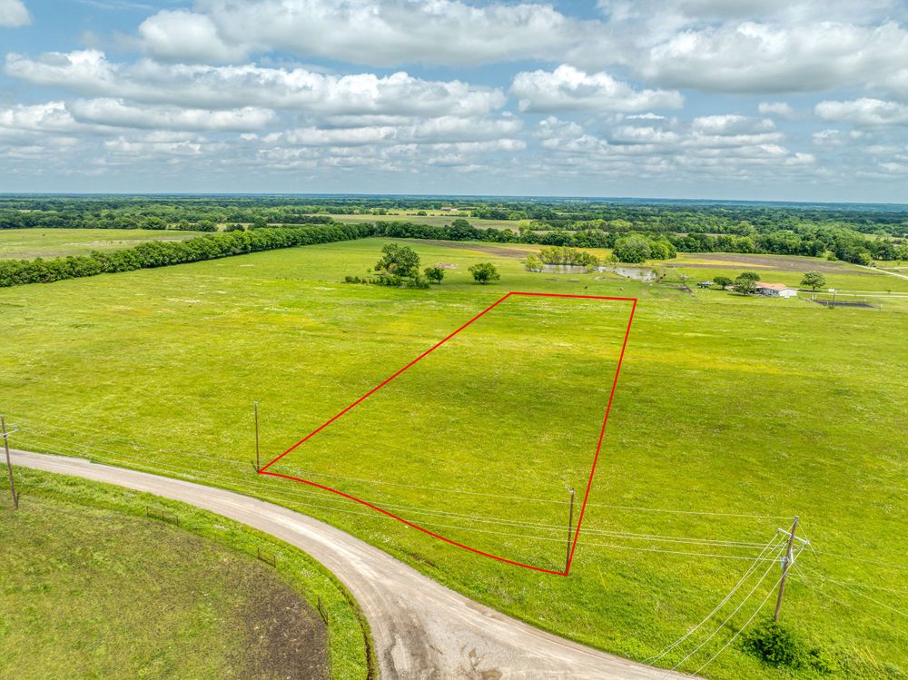 Aerial view of green pasture land with red property boundary markers outlining available lots.