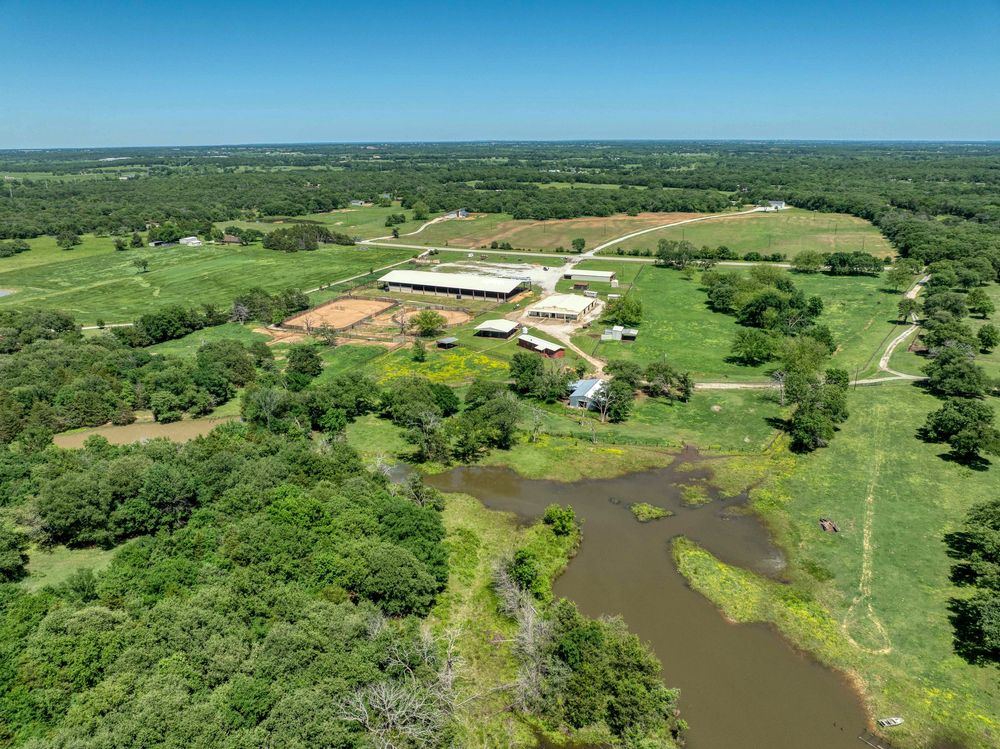 Aerial view of a ranch property with buildings and a pond nestled in rolling green countryside.