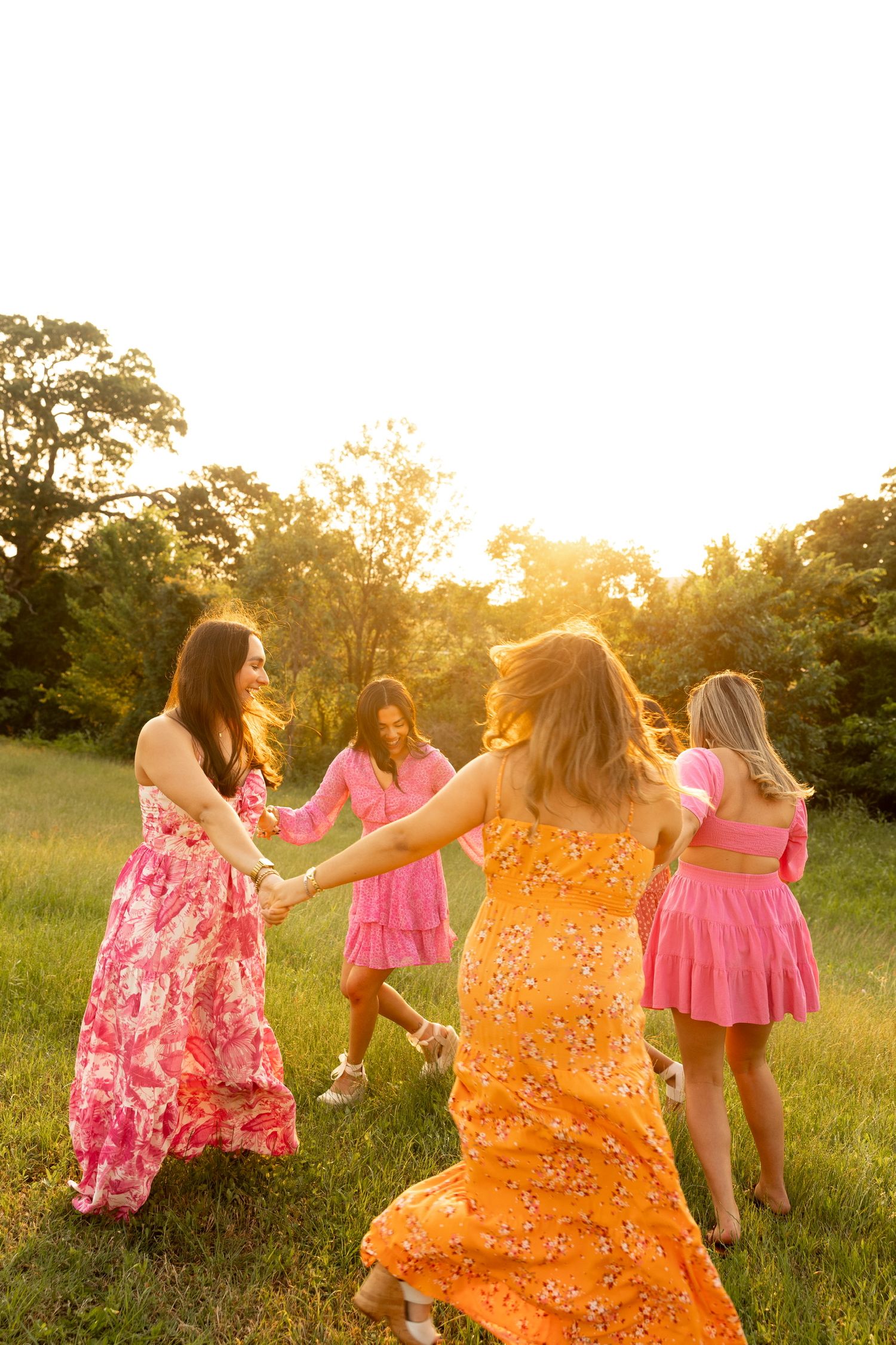 Group of women in colorful summer dresses dance together in field during golden hour.