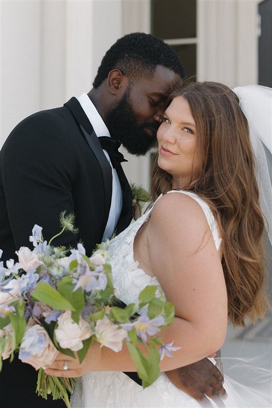 Intimate moment between newlyweds with bride holding delicate pastel floral bouquet.