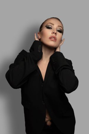 Fashion portrait of a woman in an oversized black blazer with dramatic smoky eye makeup on gray background.