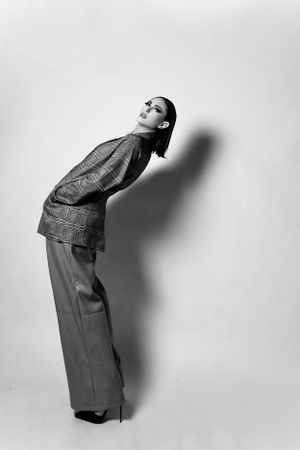 Black and white fashion photo of a woman in wide-leg trousers and textured top leaning against a wall.