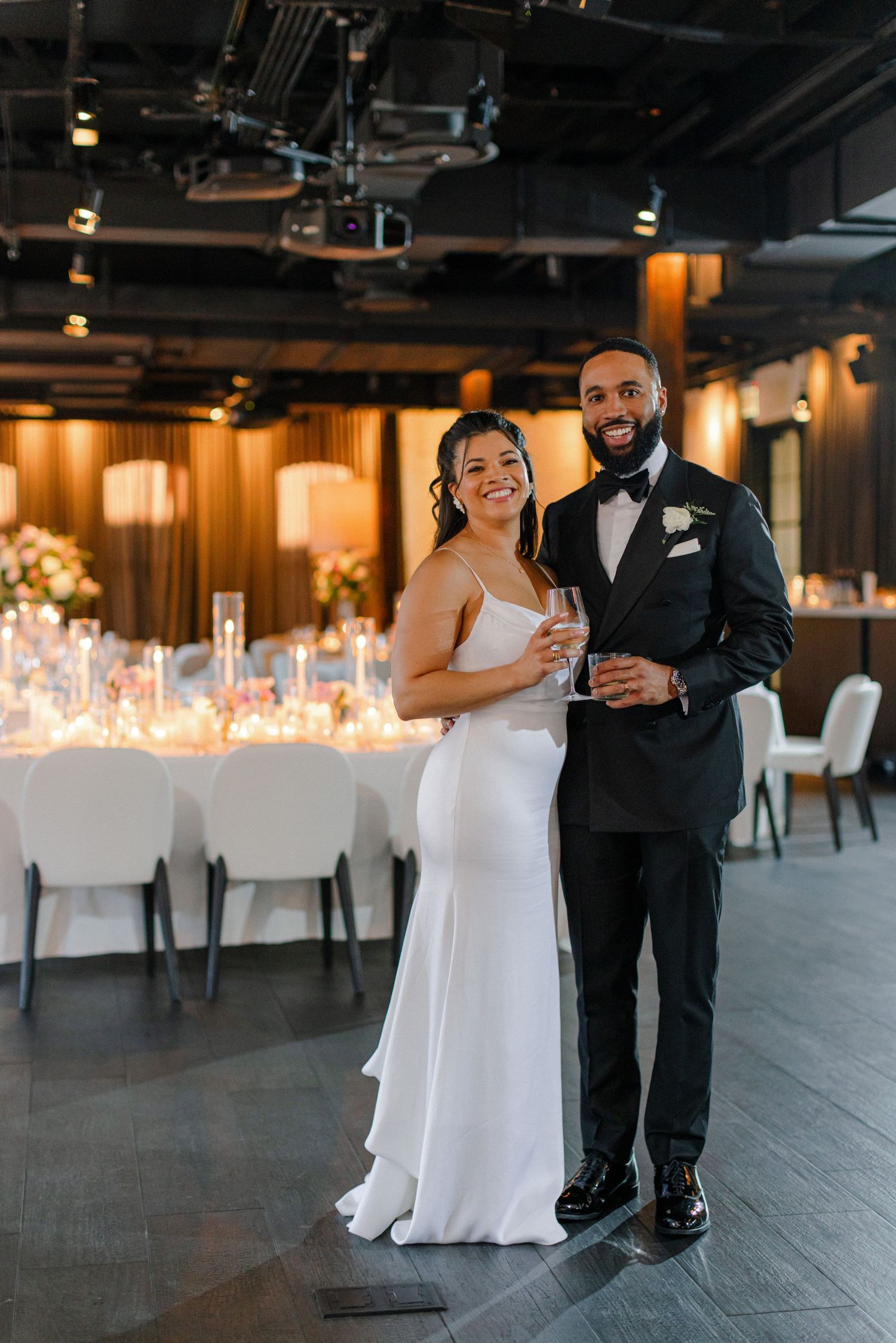 An elegant wedding reception venue with candlelit tables and modern industrial ceiling details.