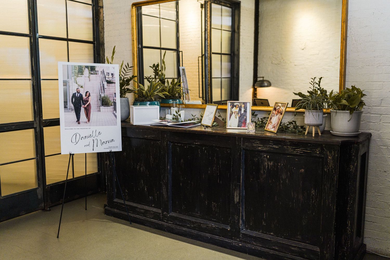 Wedding reception entry table with display photos and decor against black paneled wall.