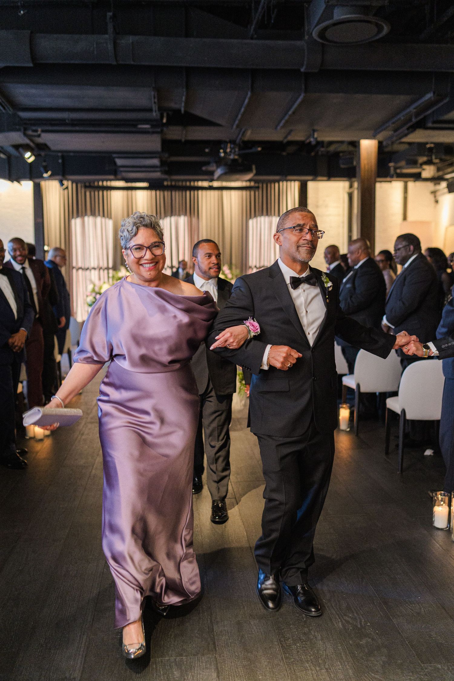 Wedding guests dancing in formal attire at reception in modern venue.