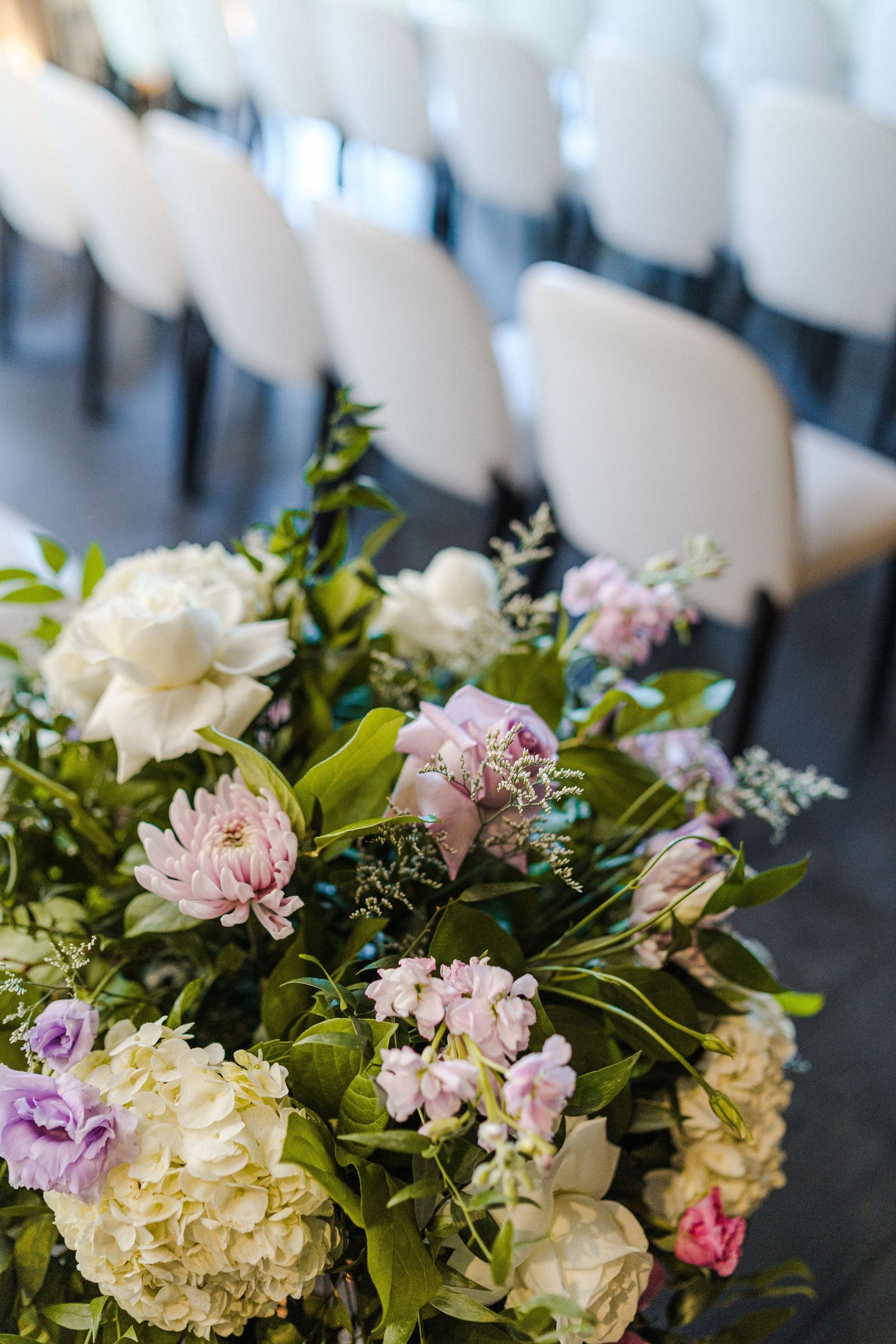 Elegant floral arrangement with pink and white flowers against backdrop of white chairs.