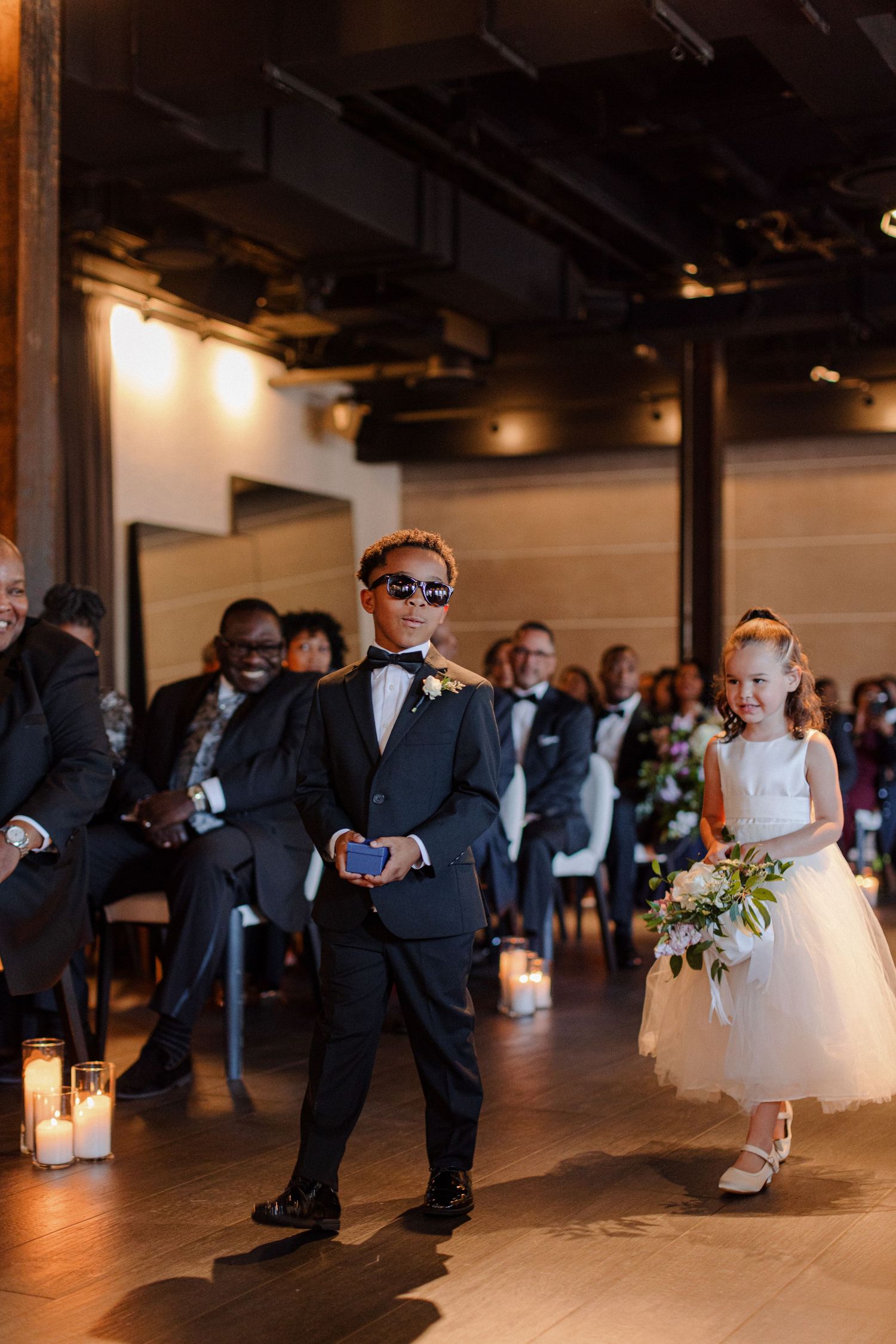 Wedding processional in modern venue with ring bearer walking down candlelit aisle.