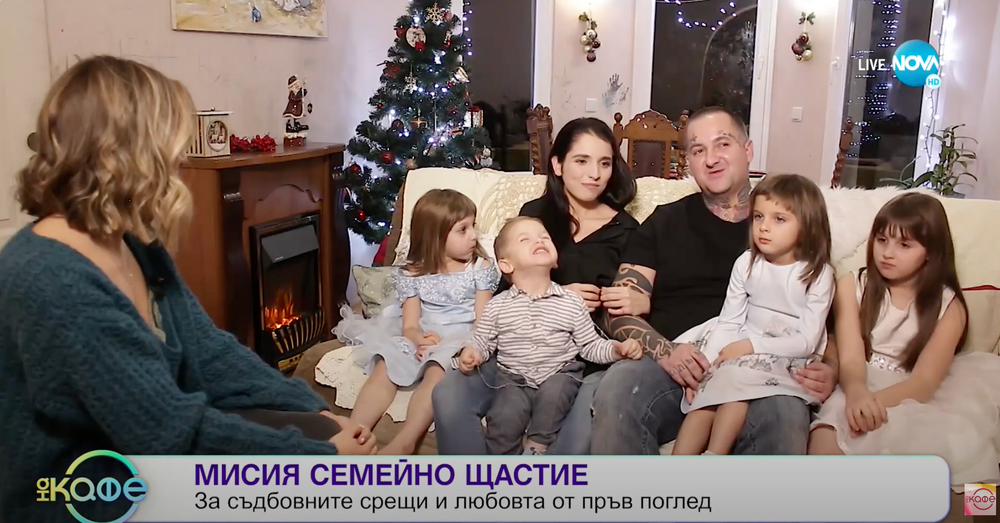 Family sitting together on couch near Christmas tree and fireplace during television interview.