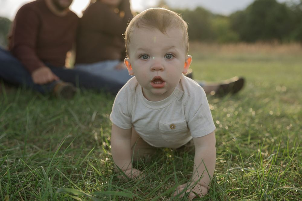Baby in light colored onesie crawling on grass during golden hour.