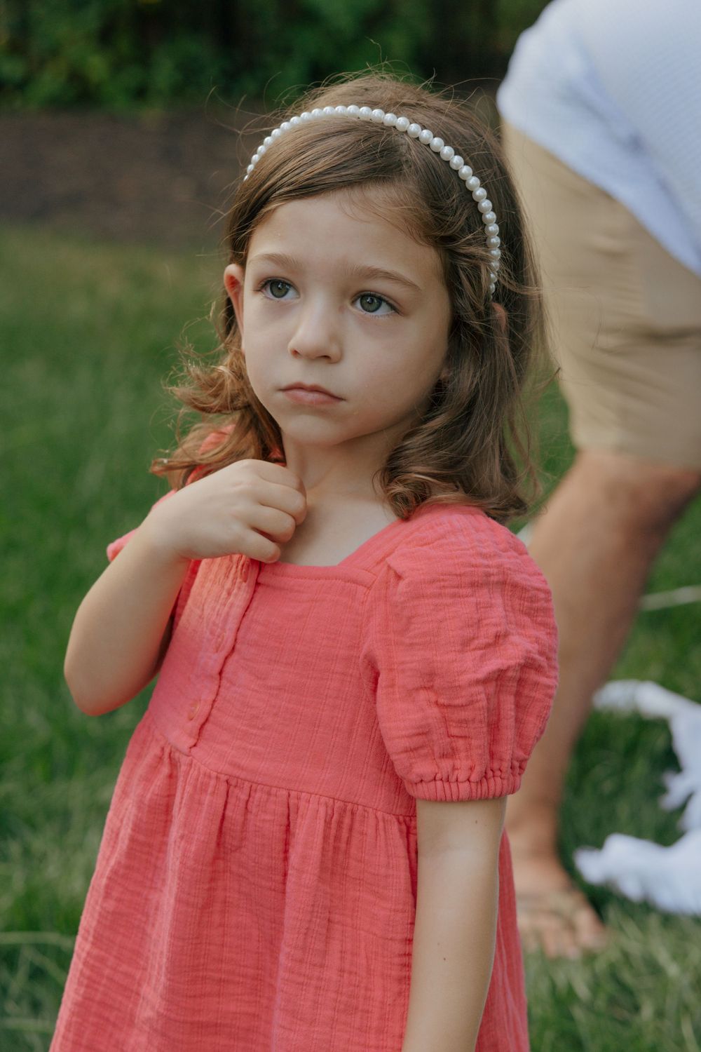 Person in a coral dress and pearl headband poses outdoors.