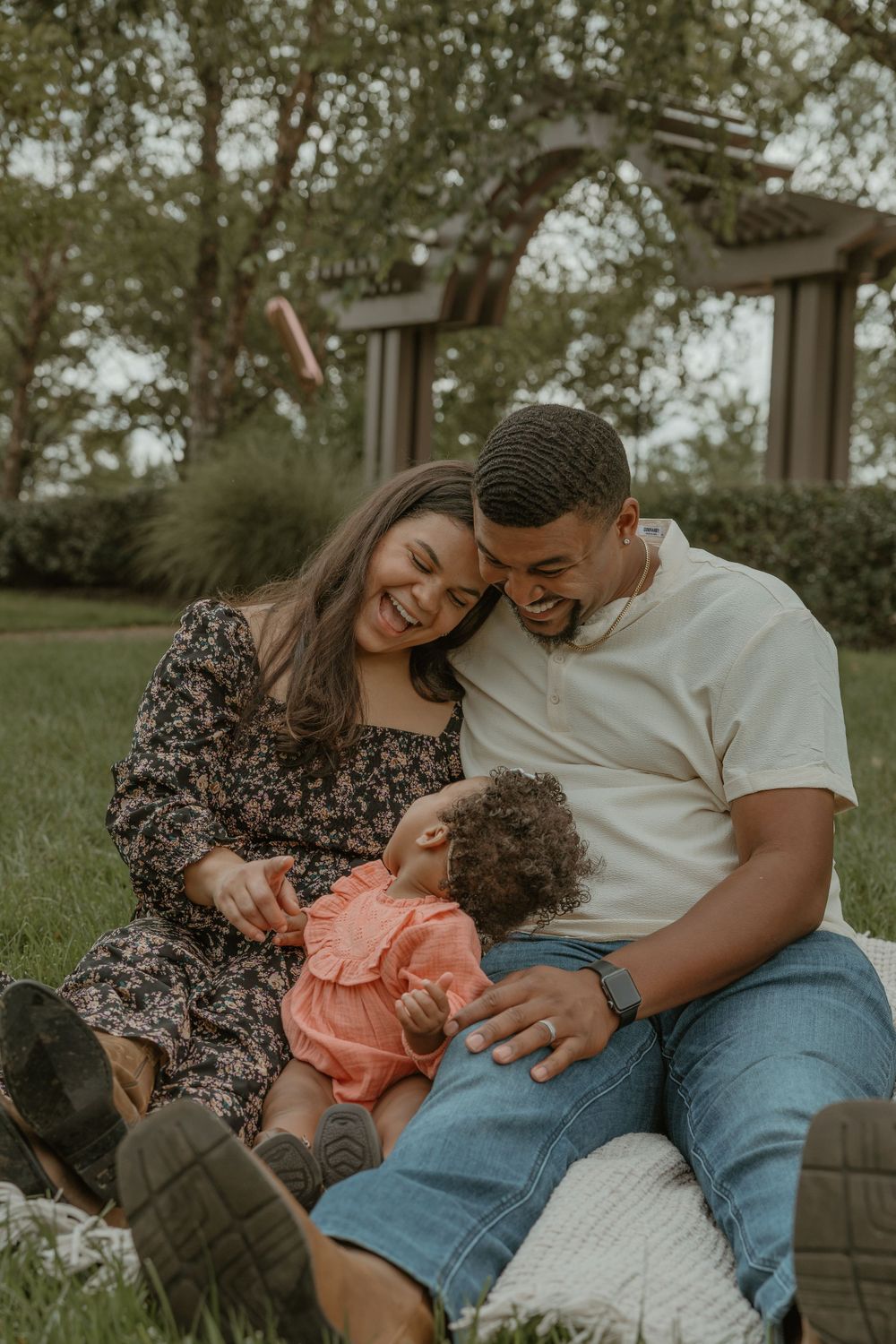 Family sharing intimate moment while relaxing on blanket in park setting.