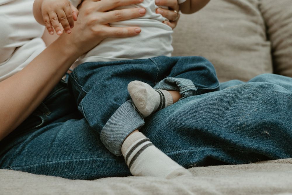 Close-up of small feet in striped socks resting on denim-clad legs on a couch.