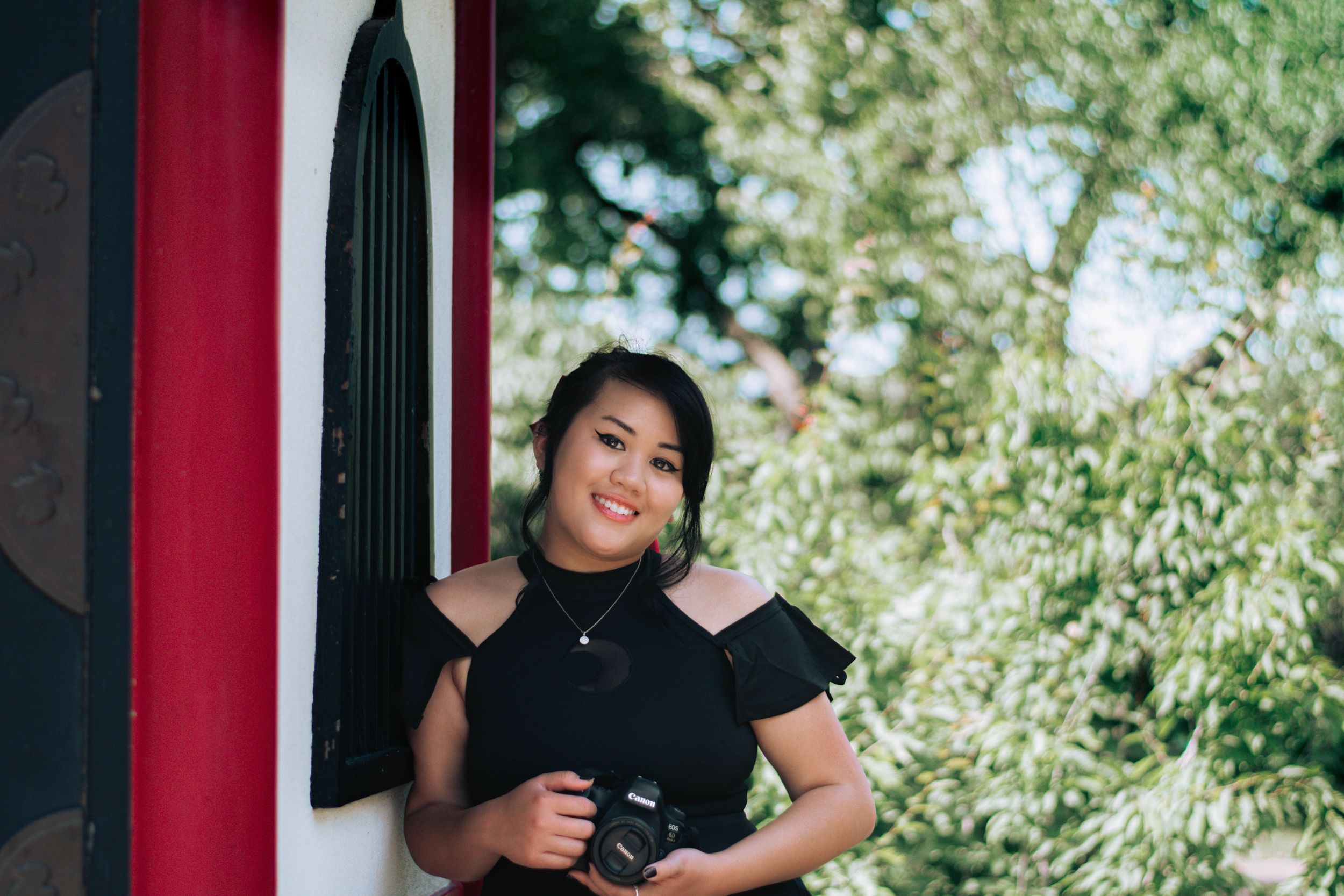 Person in black shirt poses casually against red and white striped background outdoors.