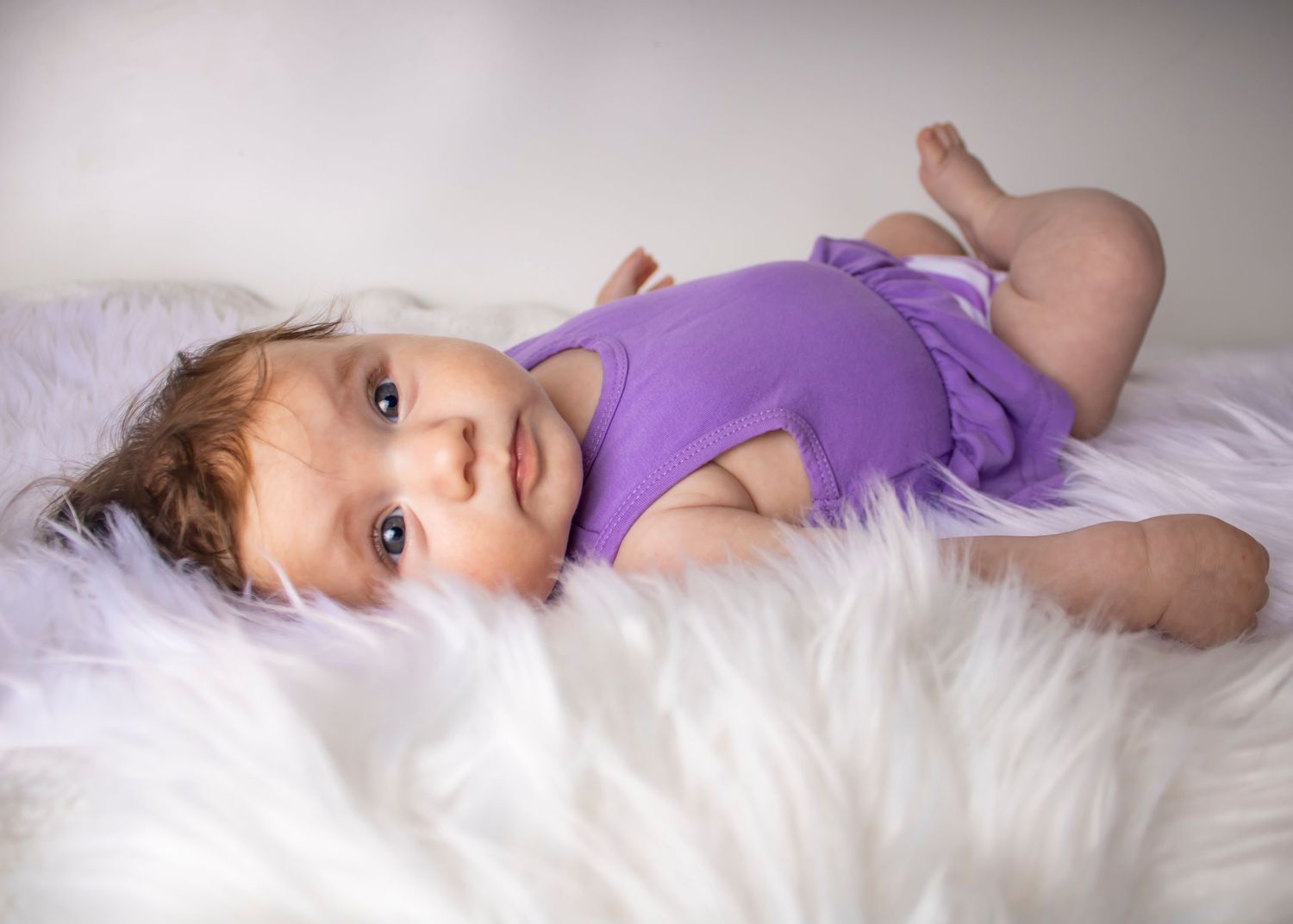 A baby girl looks over her shoulder at the photographer, she is lying on her back