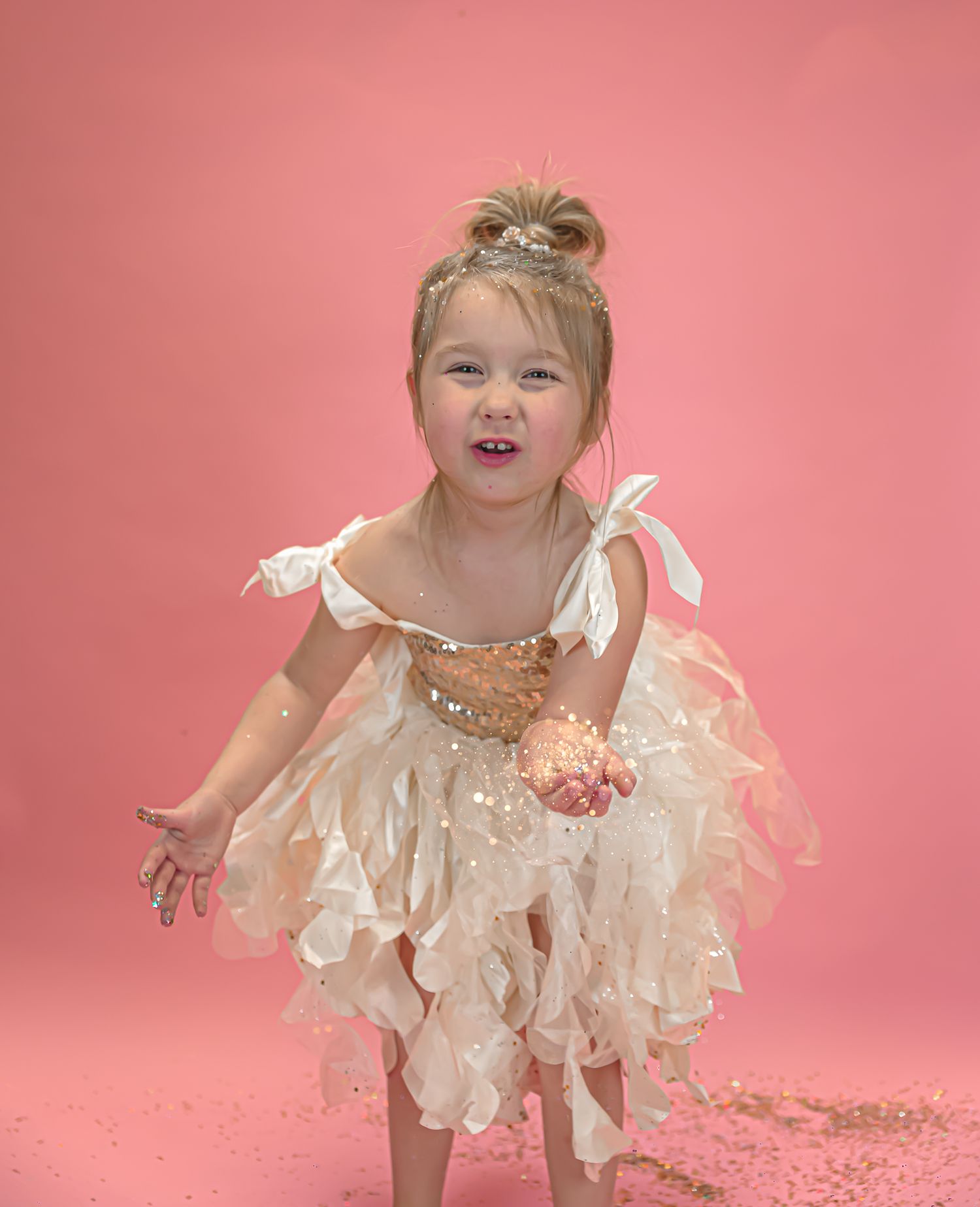 Celebratory portrait in a ruffled cream dress with glitter against a pink background.