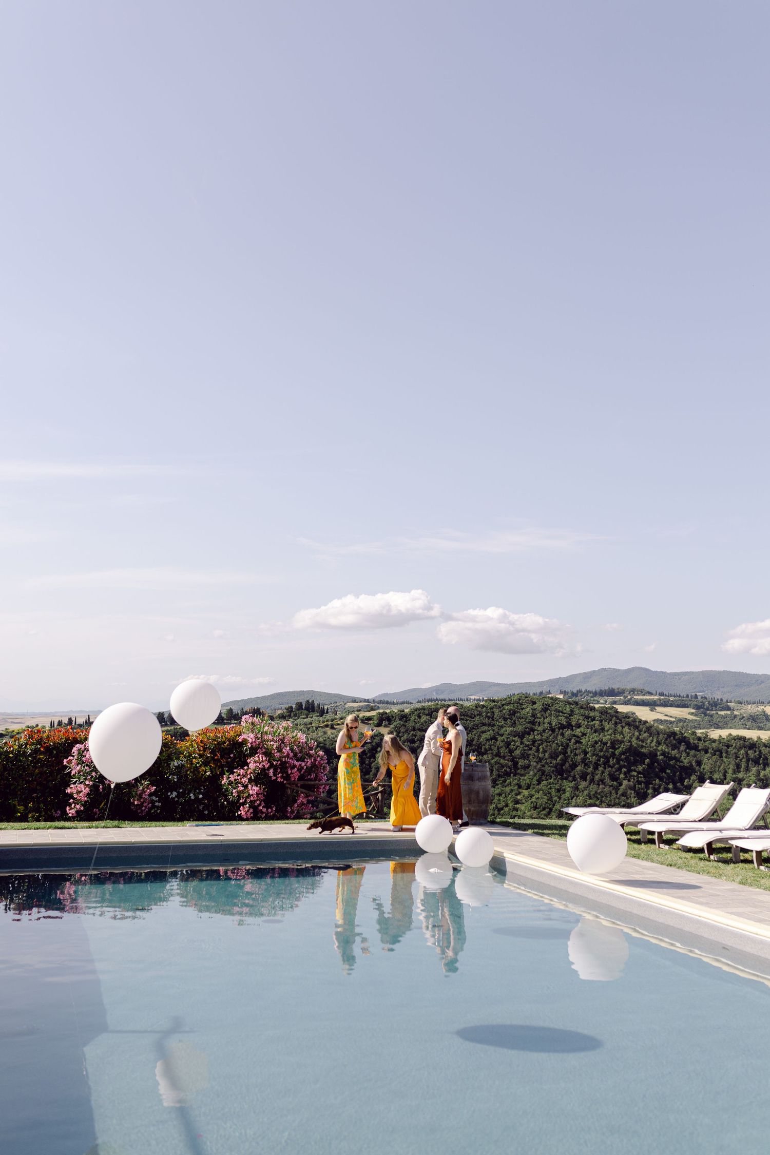 Wedding guests stand beside a pool overlooking scenic Tuscany views at an Italian Tuscany destination wedding.