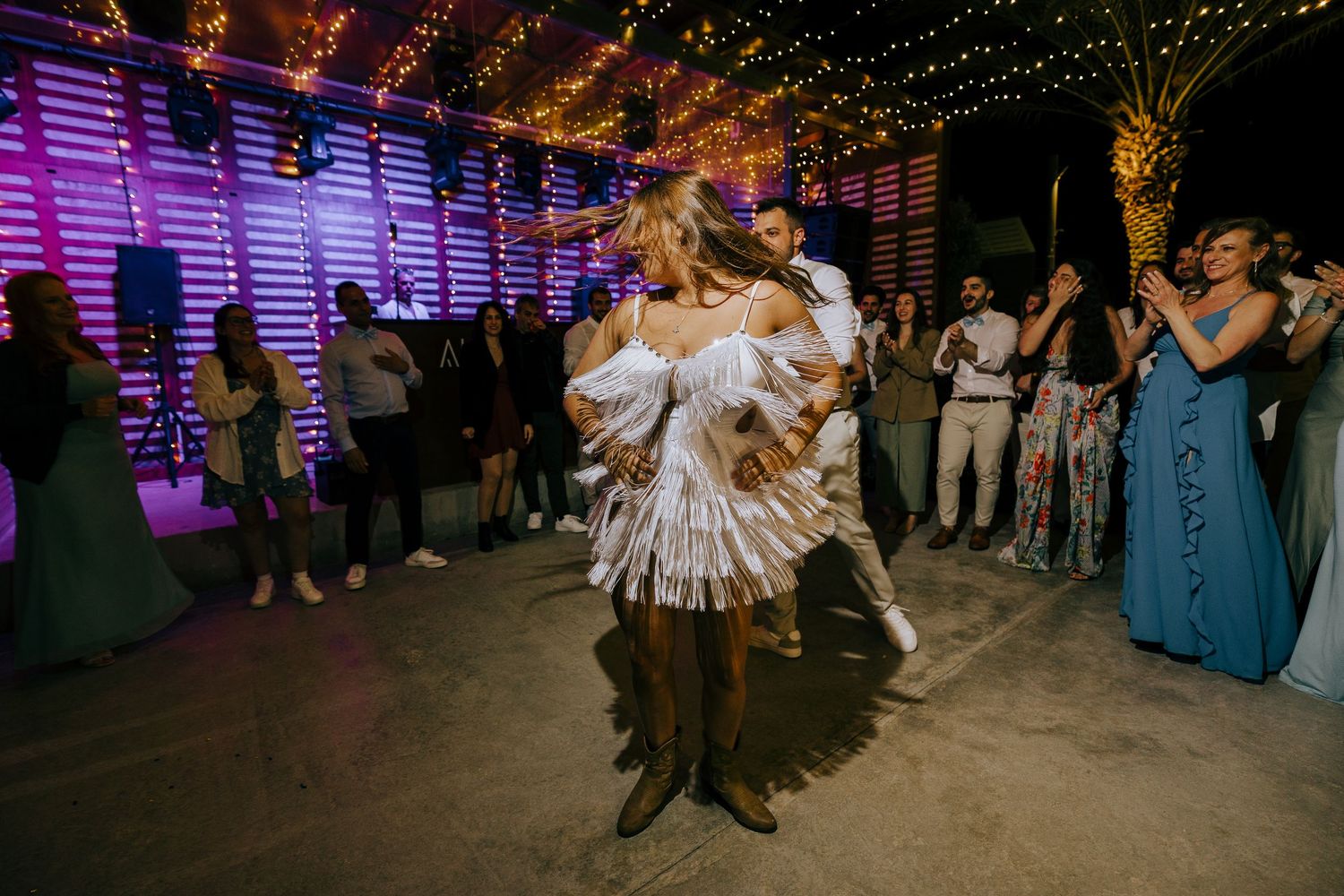 A couple dancing at a wedding reception under purple lighting with guests watching in the background.