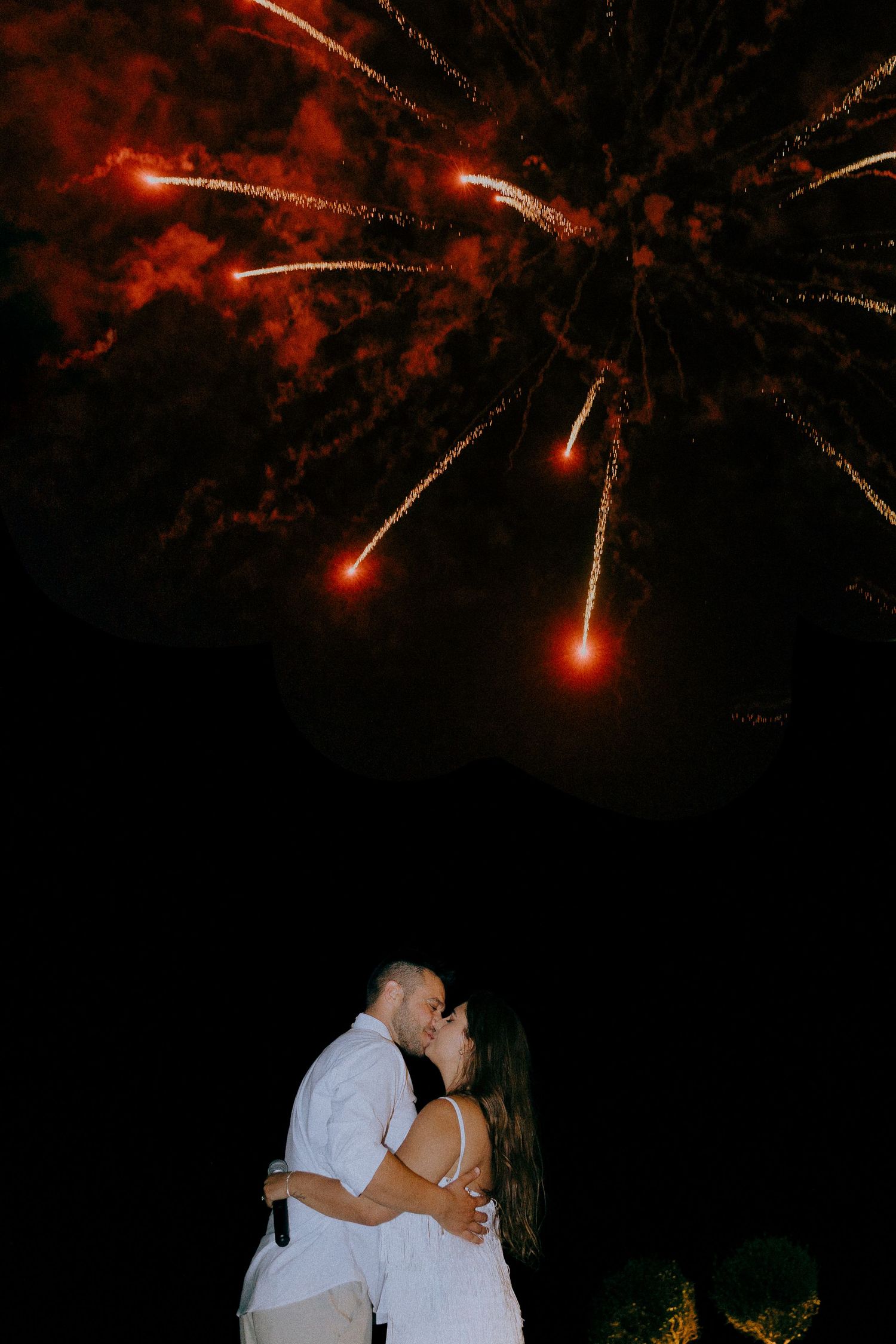 A romantic moment under red fireworks exploding in the night sky.