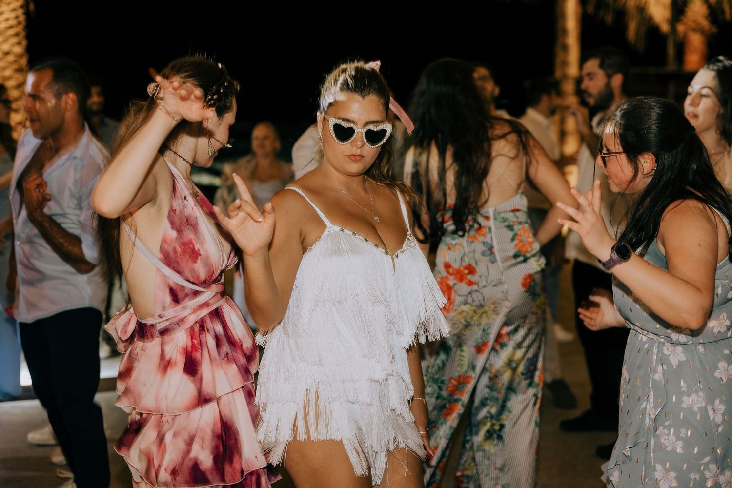 A group of people dancing and celebrating at a party wearing colorful dresses and summer outfits.