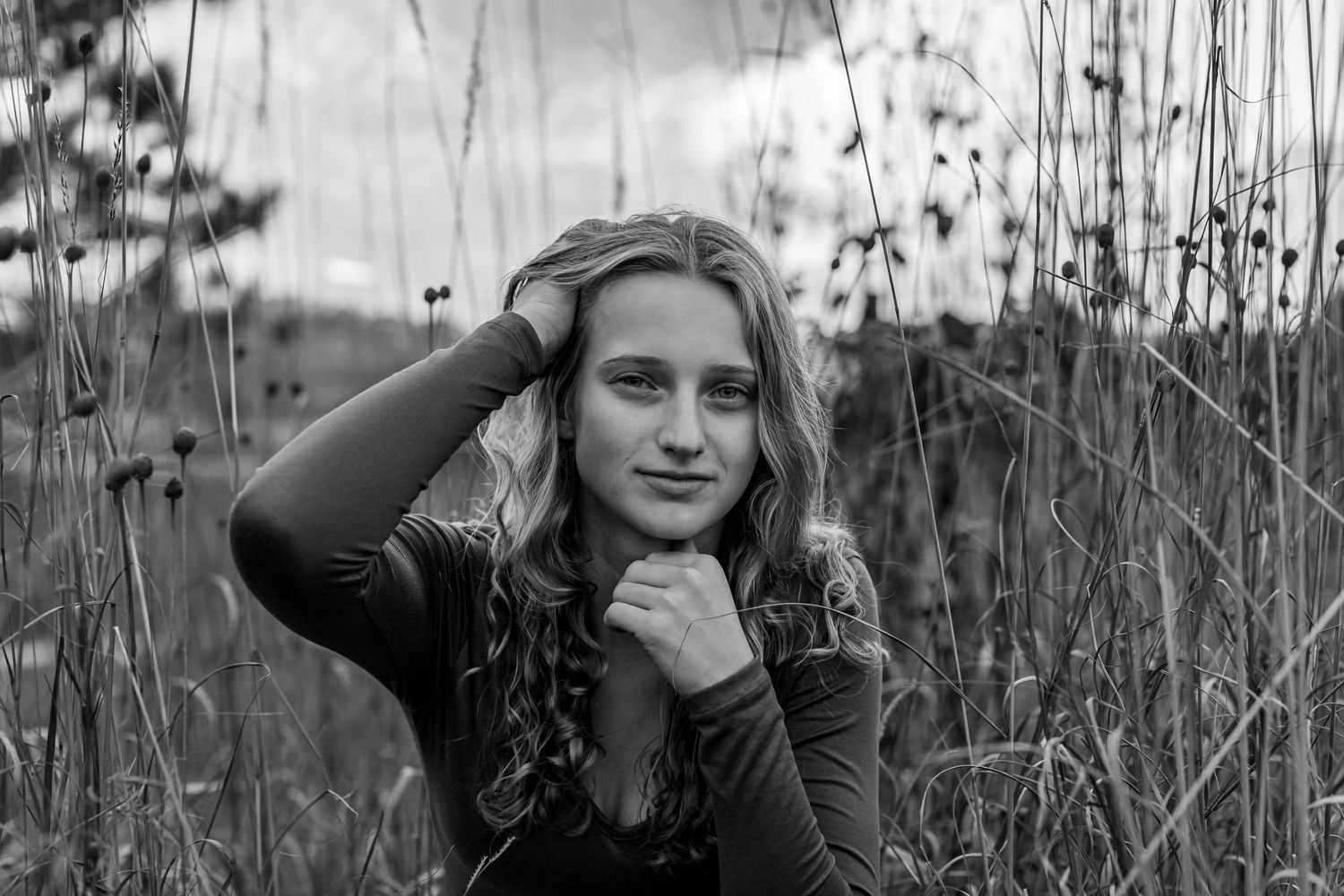 People posing together in tall grass field during moody black and white photoshoot.