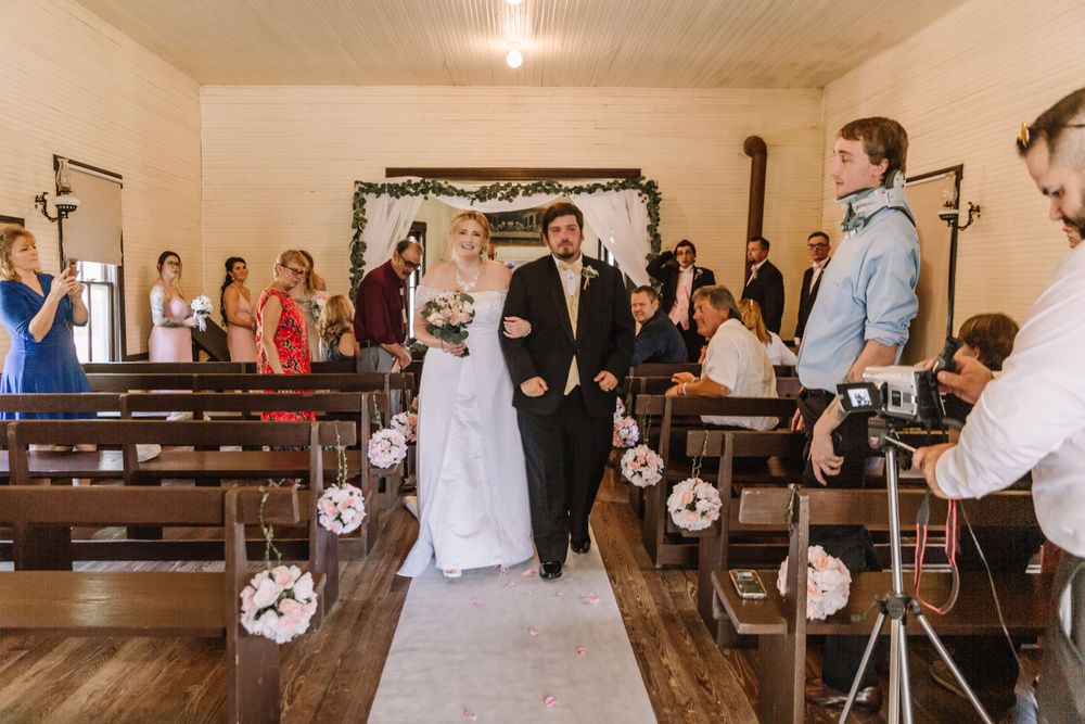 Indoor wedding ceremony in rustic chapel with wooden pews and hanging lantern decor.