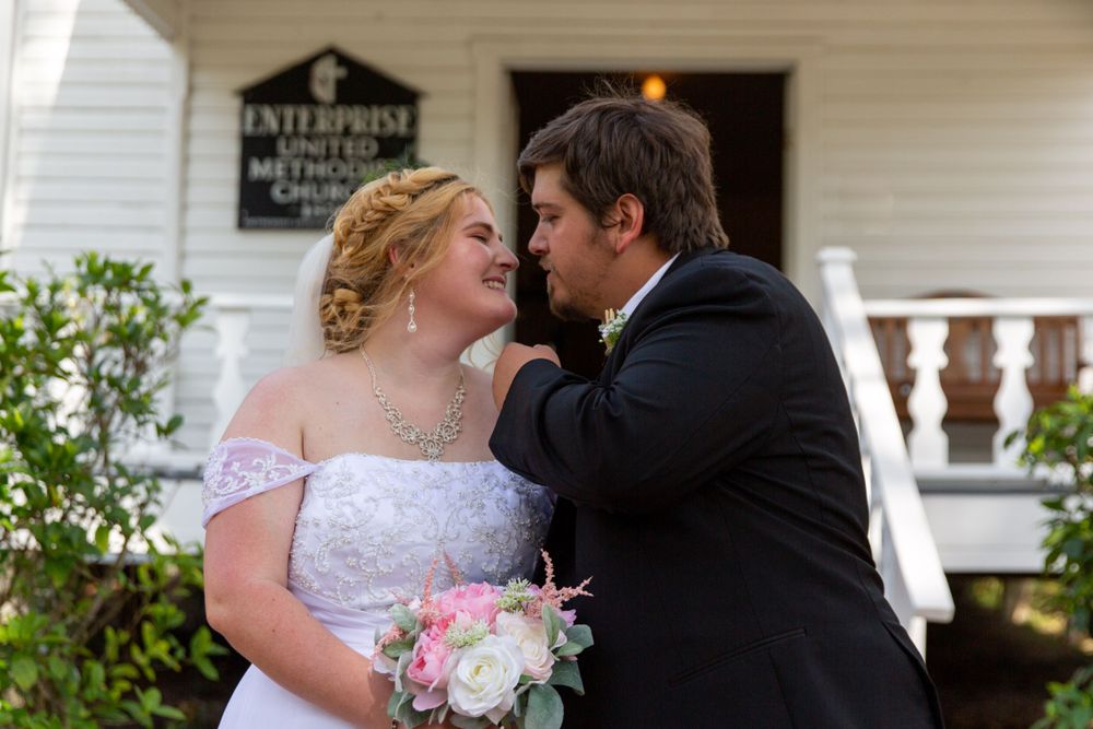 A romantic wedding kiss on the porch of a historic white building with a classic architecture backdrop.