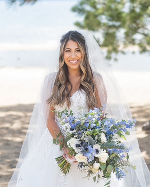 Happy bride standing by Lake Tahoe holding a huge white and blue flower bouquet