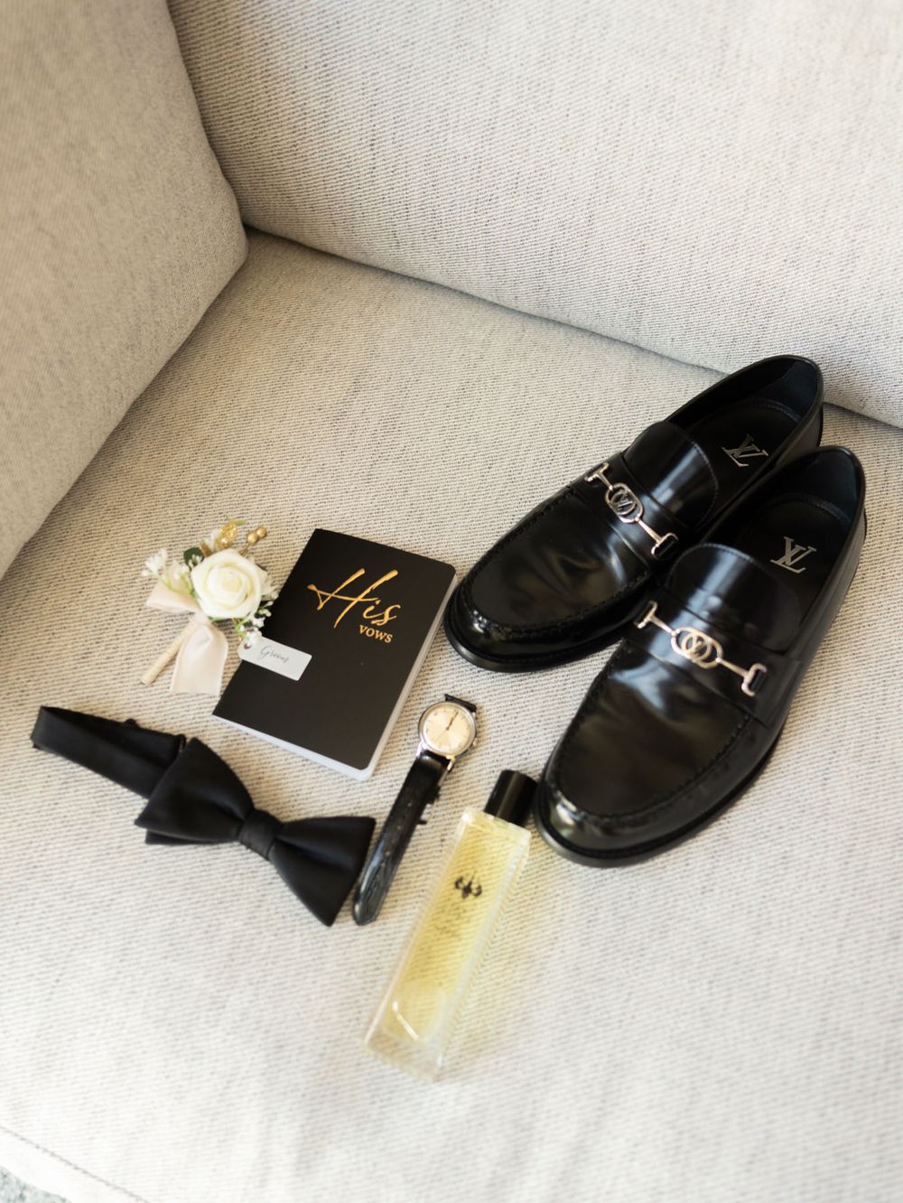 Elegant black leather dress shoes displayed with perfume bottle and accessories on a light gray couch.