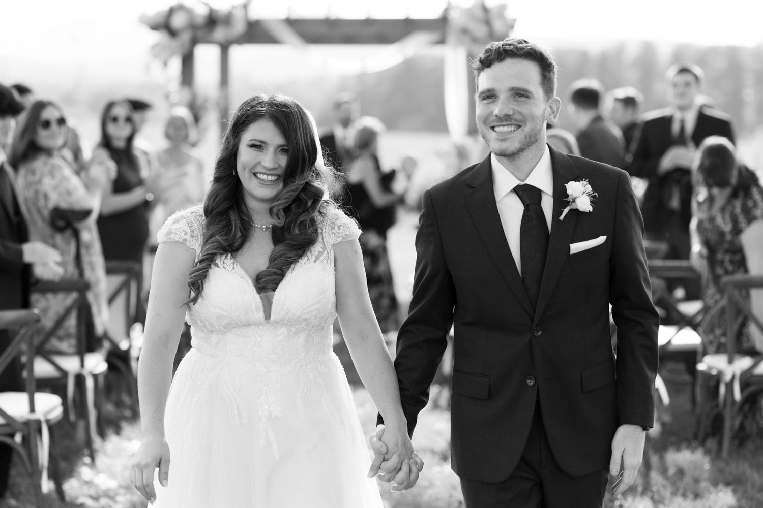 A black and white wedding ceremony photo shows a joyful couple walking down the aisle together as newlyweds.