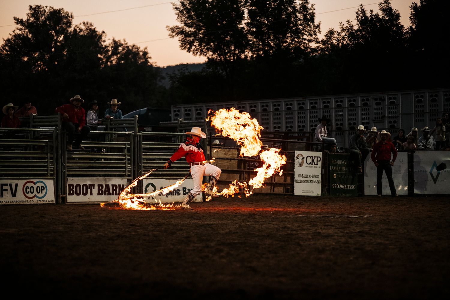Dramatic fire explosion during rodeo event at night with spectators visible in background.