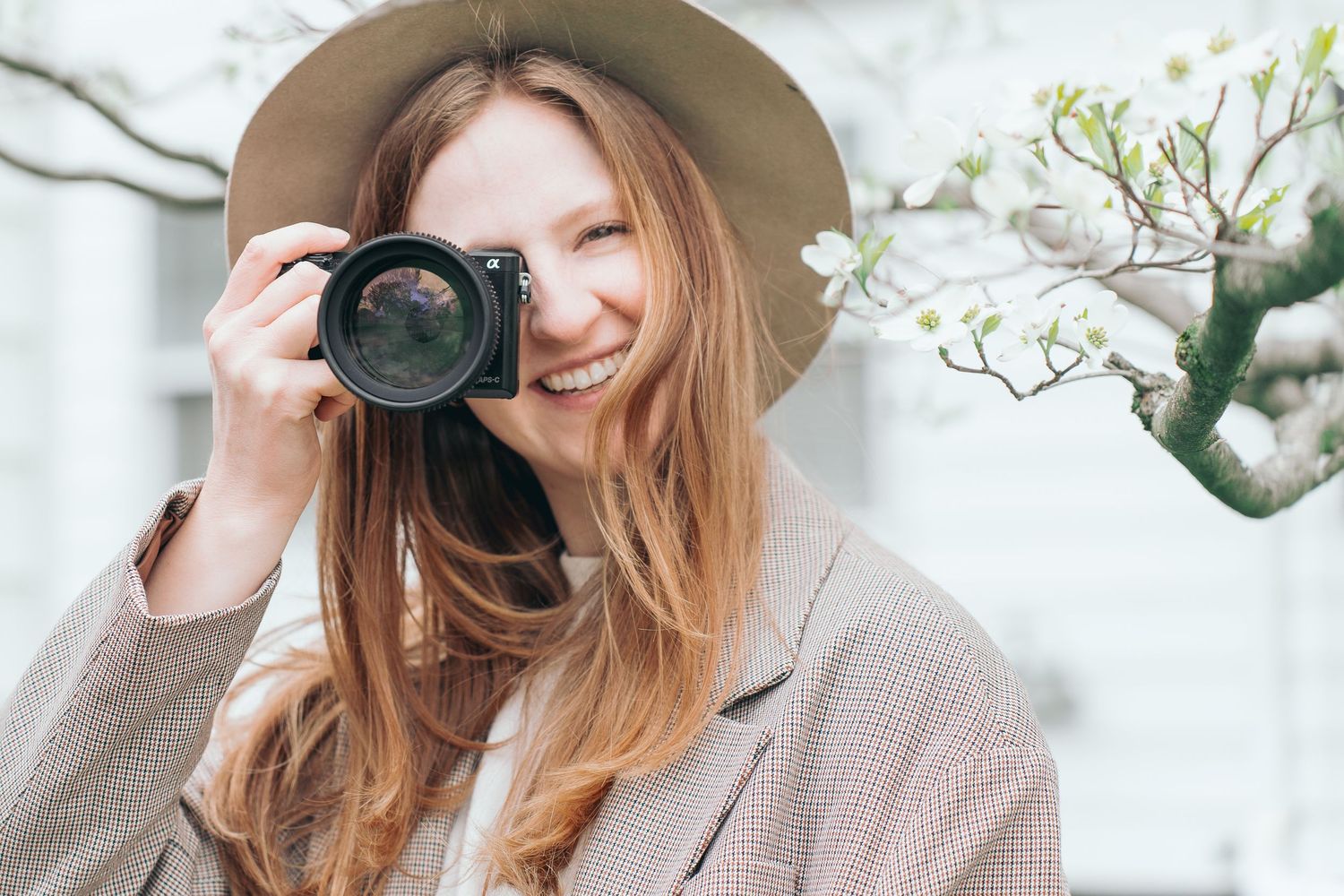 A person wearing a beige hat takes a photo with a professional camera outdoors. Cuyahoga Falls, Ohio