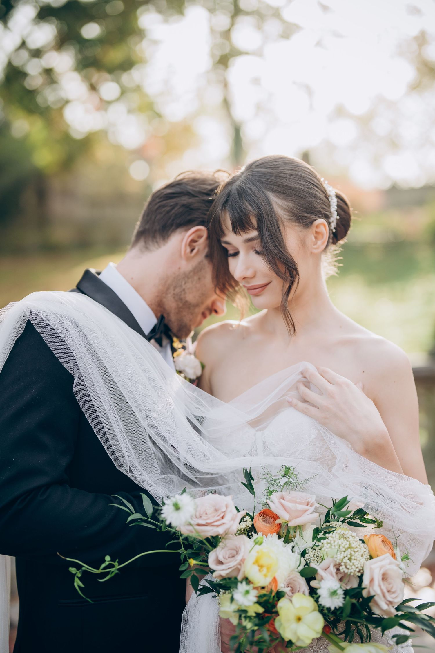 Romantic outdoor wedding moment with delicate veil and spring floral bouquet.
