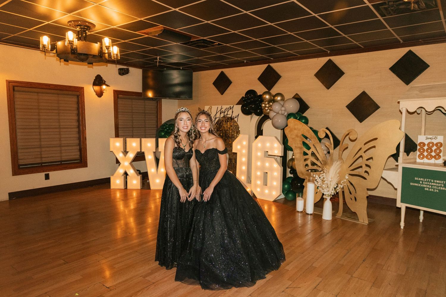 People in formal black gowns pose in a decorated indoor venue with geometric wall decor.
