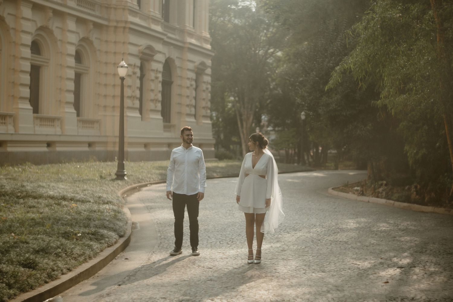 Couple walking together on a curved path outside a grand historic building on a misty morning.