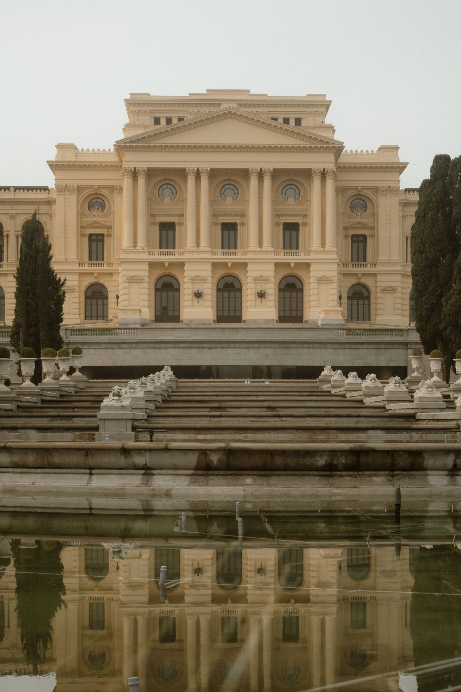 A grand classical building with ornate architecture reflects in a symmetrical pool.