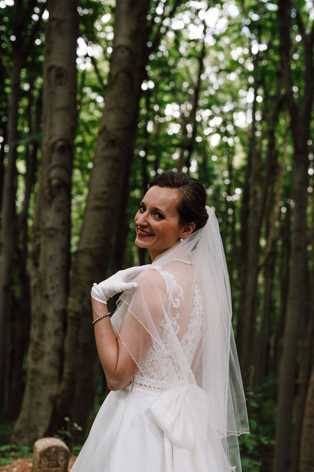 Wedding dress and veil captured in natural woodland setting.
