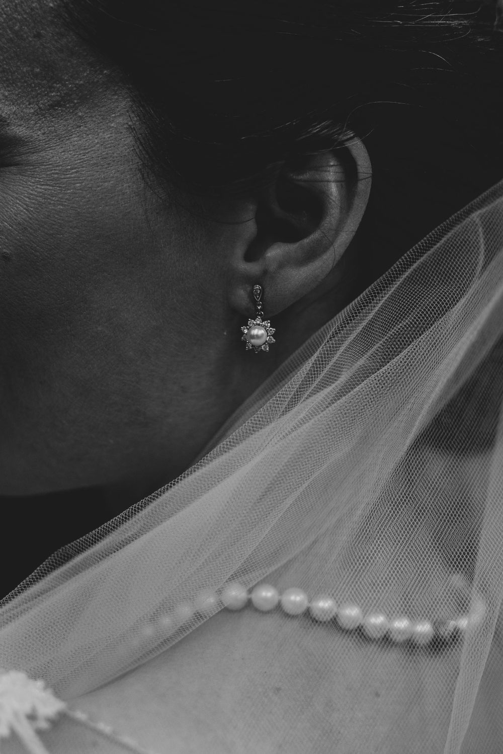 Black and white detail shot of pearl necklace and crystal earring with wedding veil.