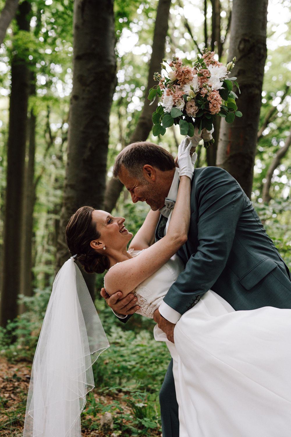 Romantic dip pose with floral bouquet in woodland setting.