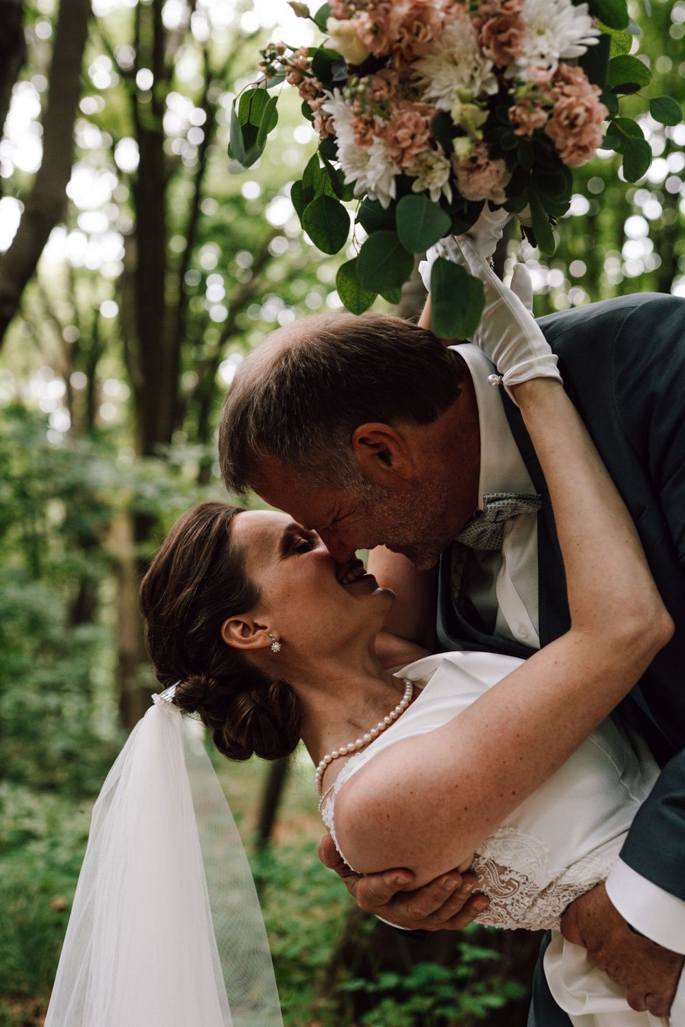 Intimate wedding moment with floral bouquet in forest backdrop.
