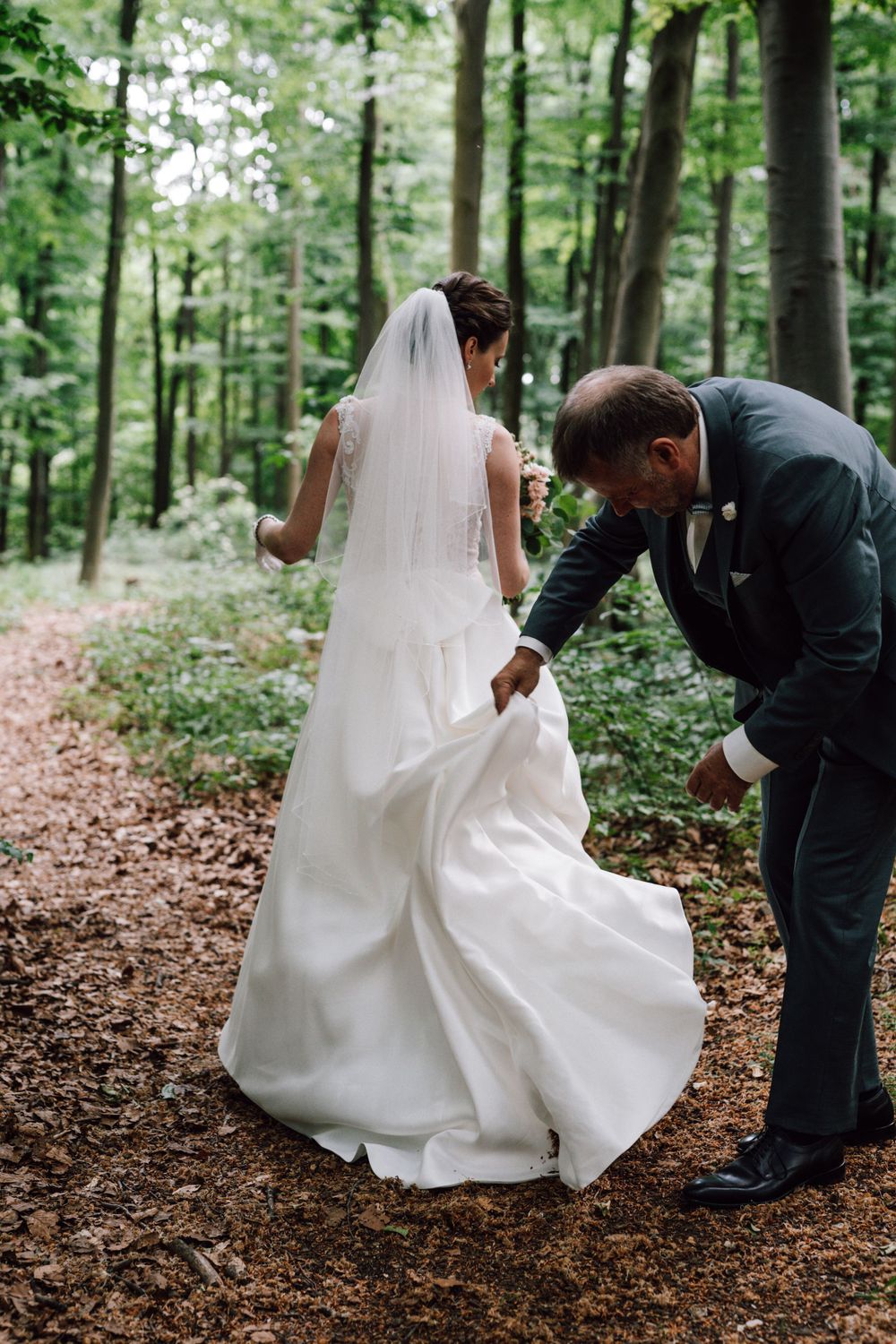 Wedding dress train being adjusted on forest path.
