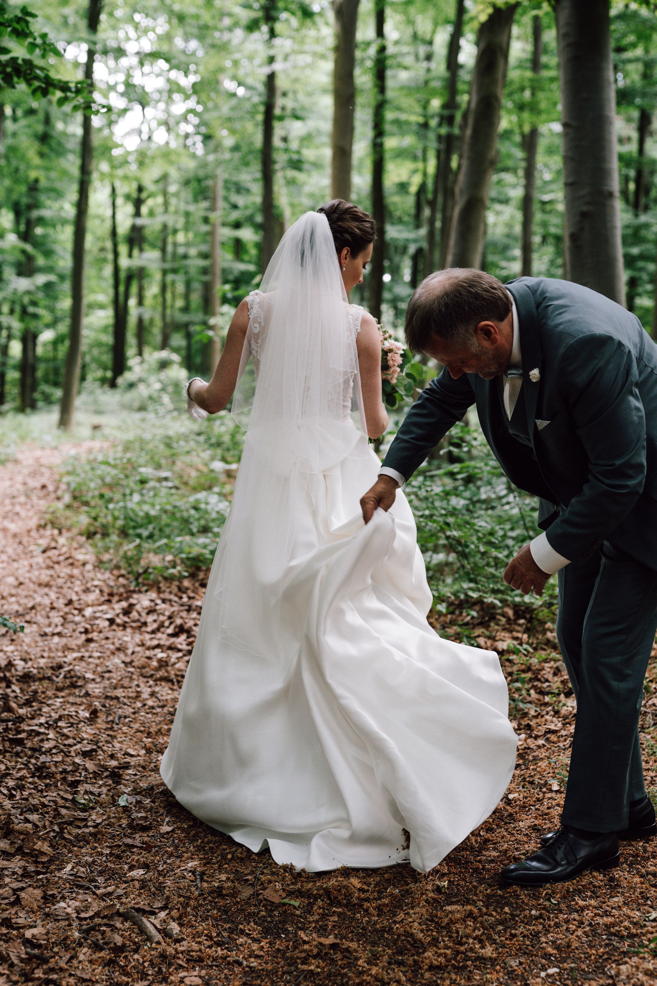 Wedding dress train being adjusted on forest path.